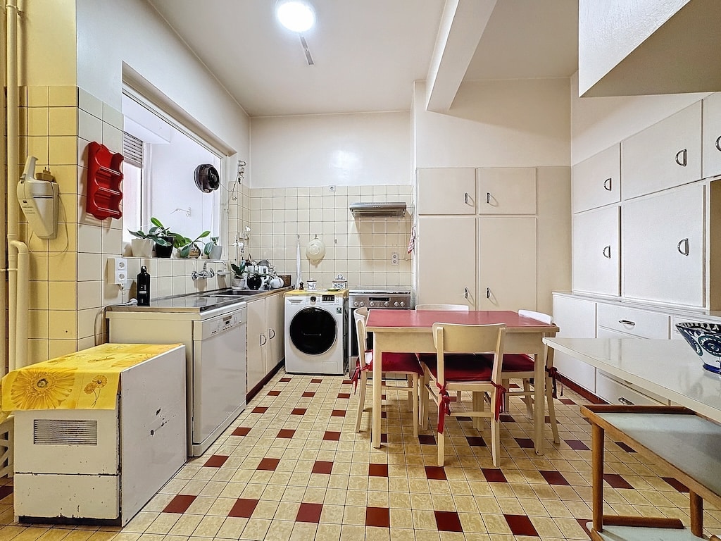 Cuisine lumineuse et pratique avec coin repas, lave-linge intégré, plantes et mobilier simple.