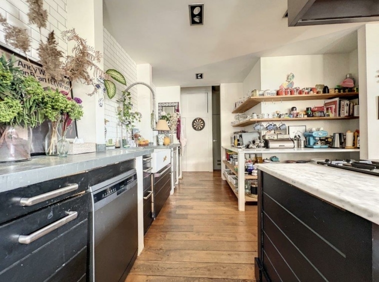 Cuisine moderne avec mobilier noir, îlot marbre, étagères colorées et touches naturelles.