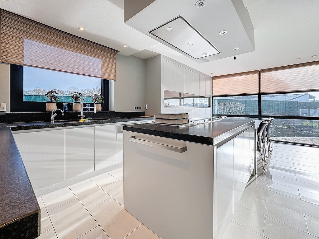 Cuisine moderne avec îlot en granit sombre, luminaires élégants et grande fenêtre panoramique.