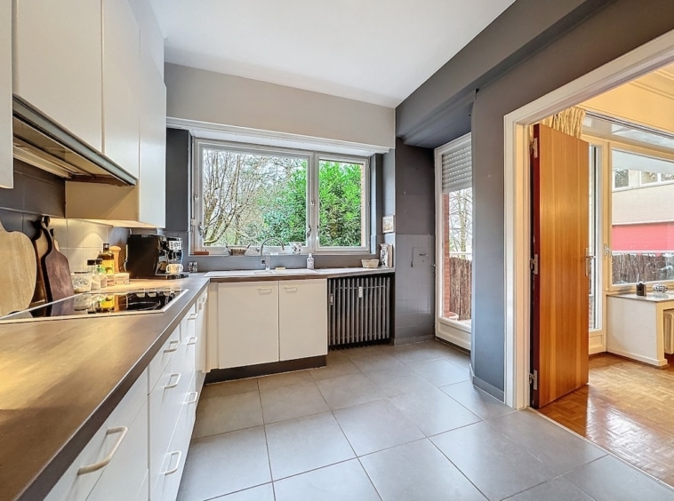 Cuisine moderne lumineuse avec vue sur la nature, mobilier blanc et accents en bois.