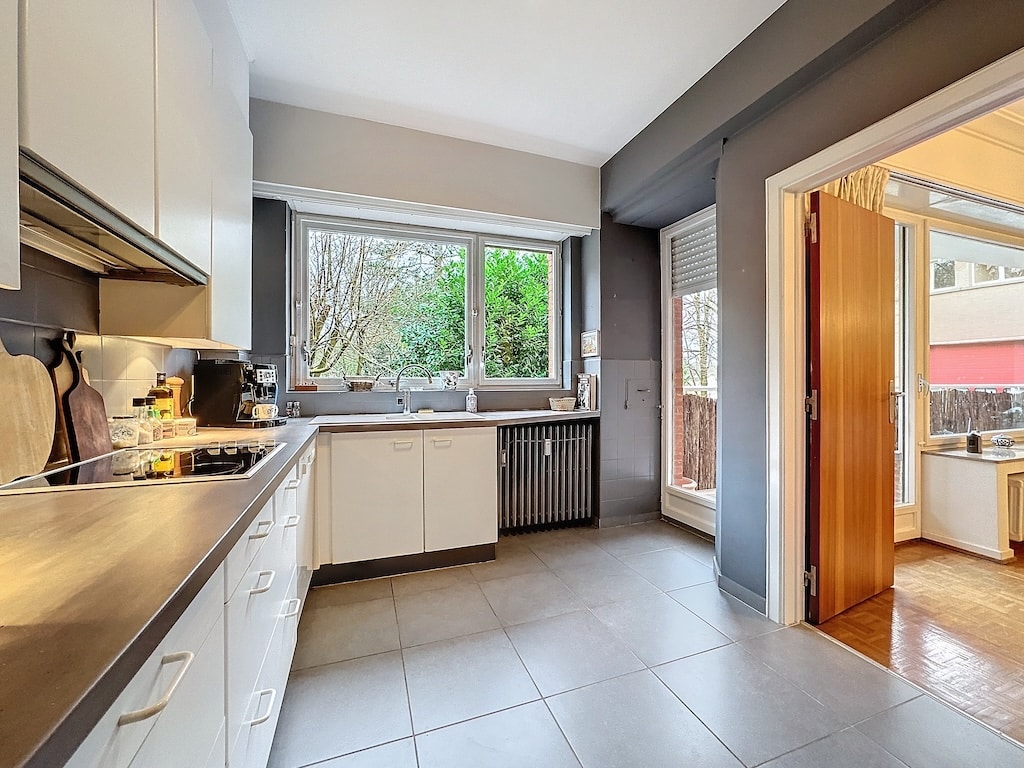 Cuisine moderne lumineuse avec vue sur la nature, mobilier blanc et accents en bois.