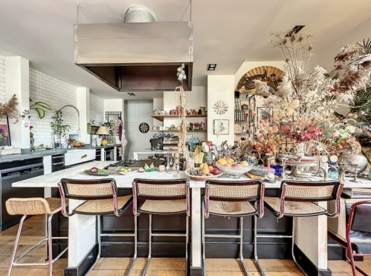Cuisine moderne colorée avec îlot central, plantes, fruits, et design éclectique chaleureux.
