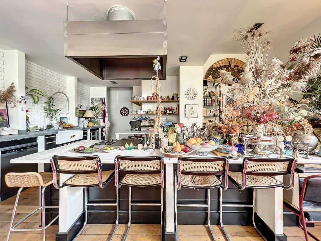 Cuisine moderne colorée avec îlot central, plantes, fruits, et design éclectique chaleureux.