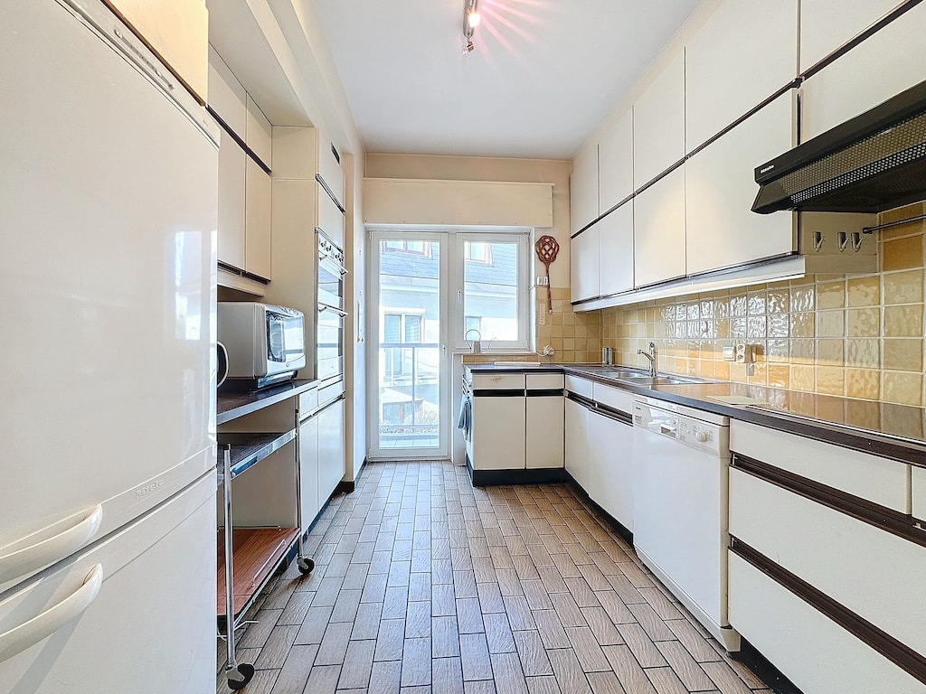Cuisine moderne lumineuse avec rangement optimisé, arrière-plan chaleureux et accès extérieur.