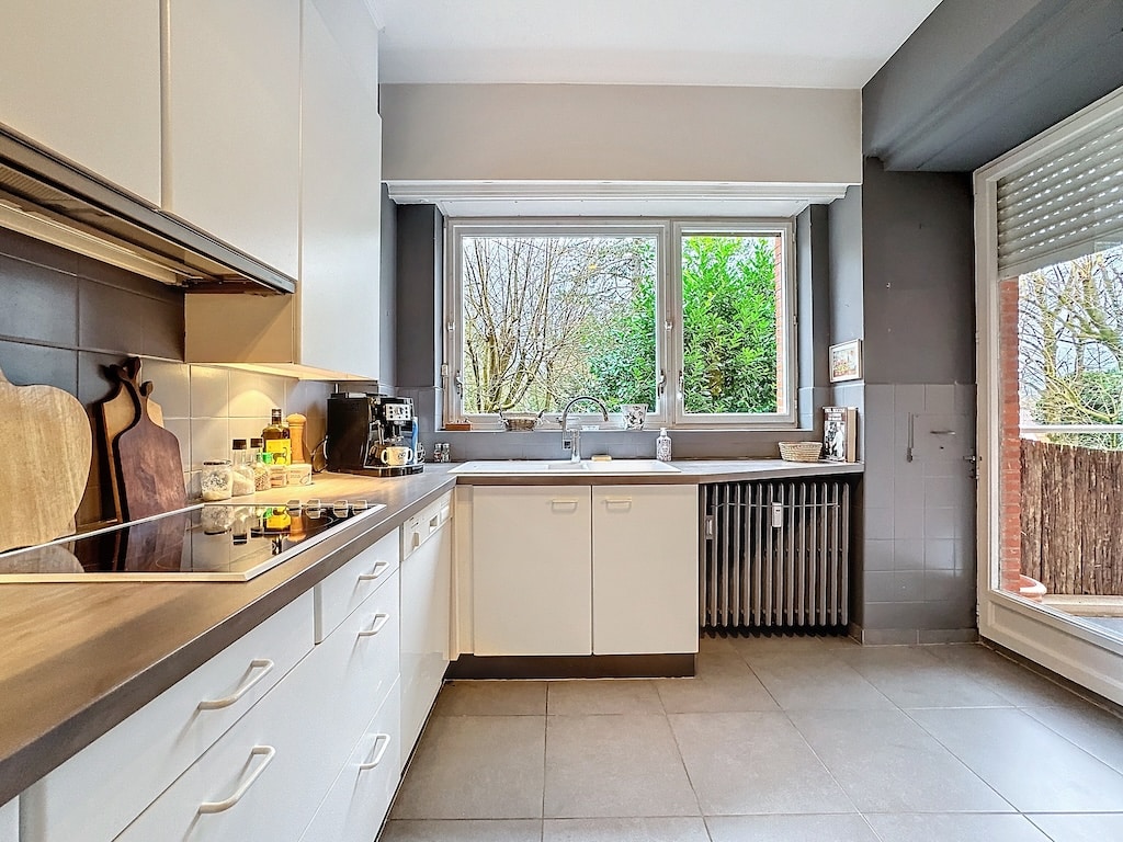 Cuisine moderne lumineuse avec façade blanche, plan en bois et vue sur la nature.