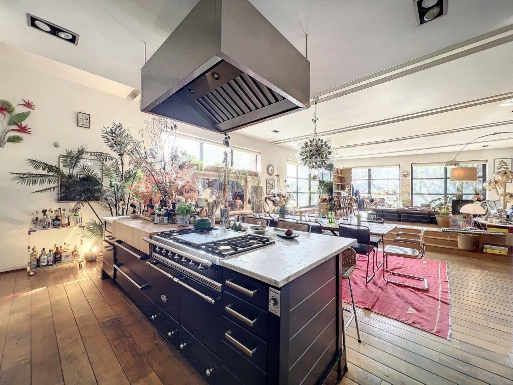 Cuisine moderne lumineuse avec îlot central en bois foncé, plantes vertes et espace convivial.