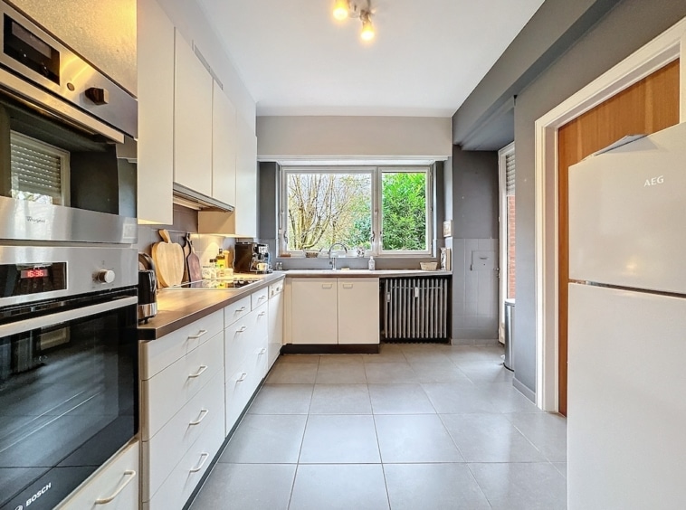Cuisine moderne lumineuse avec rangements blancs, plans sombres et vue naturelle.