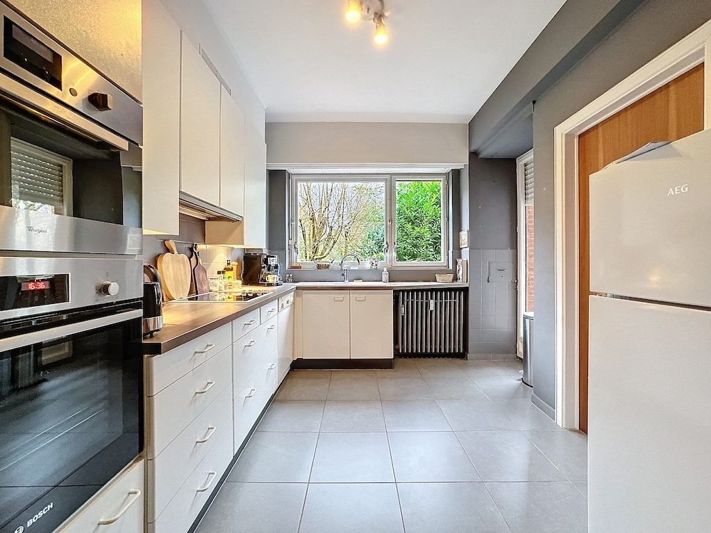 Cuisine moderne lumineuse avec rangements blancs, plans sombres et vue naturelle.