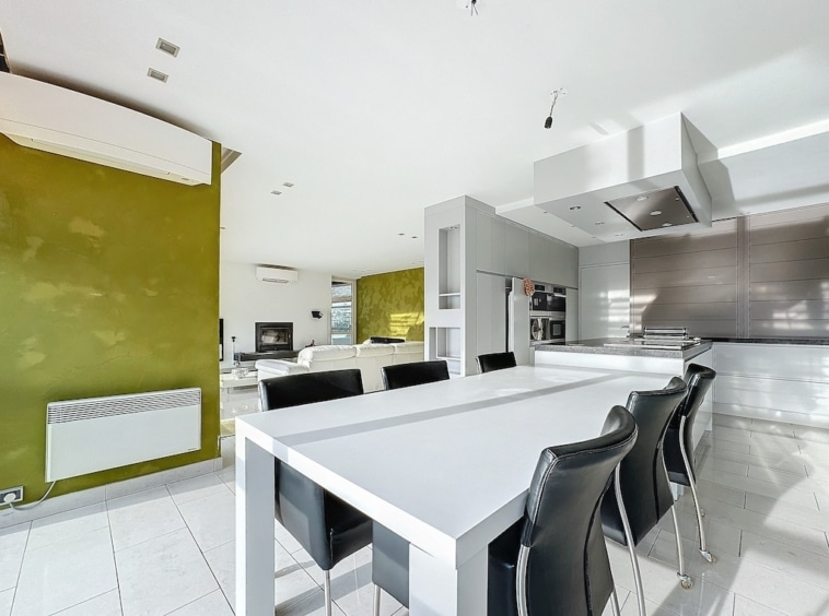 Cuisine moderne minimaliste avec murs blanc et vert olive, grande table centrale, design élégant et lumineux.