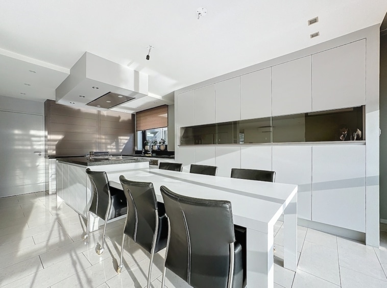 Cuisine moderne minimaliste avec îlot blanc, rangements épurés et chaises noires élégantes.