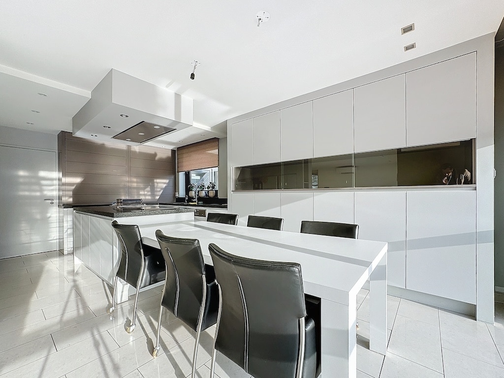Cuisine moderne minimaliste avec îlot blanc, rangements épurés et chaises noires élégantes.