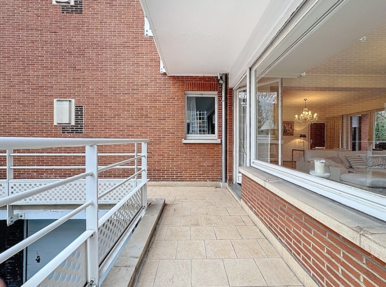 Espace extérieur moderne avec façade en brique, terrasse en carreaux et intérieur lumineux.