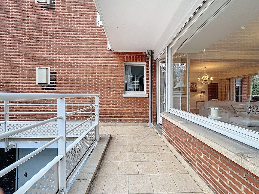 Espace extérieur moderne avec façade en brique, terrasse en carreaux et intérieur lumineux.