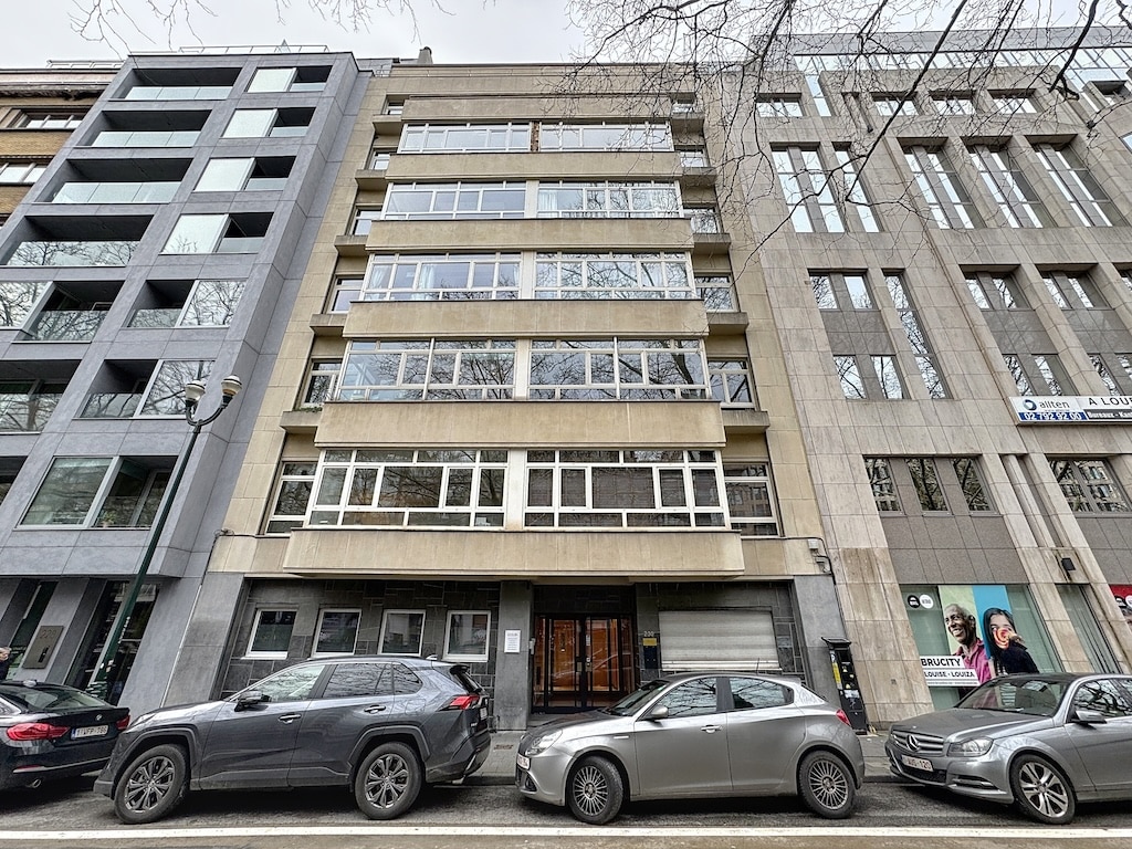Immeuble moderne en centre-ville avec façade vitrée, bâtiments variés et parking urbain élégant.