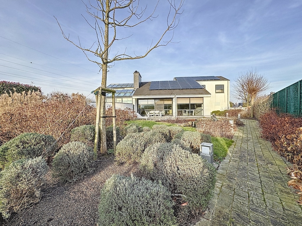 Maison moderne écologique avec jardin paisible, grandes fenêtres et panneaux solaires durables.