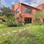Maison moderne intégrée à la nature avec jardin luxuriant, fenêtres panoramiques et toit plat épuré.