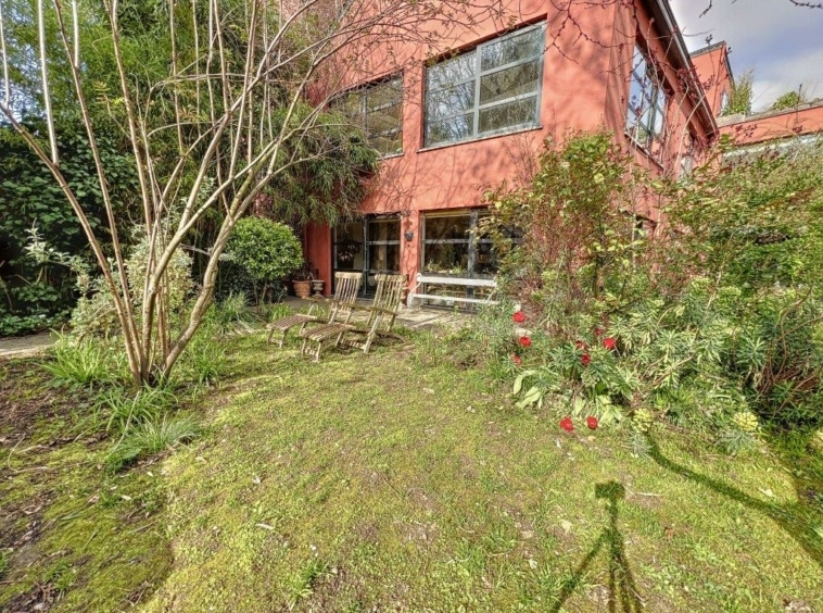 Maison rouge moderne dans un jardin verdoyant, espace paisible et propice à la détente en nature.