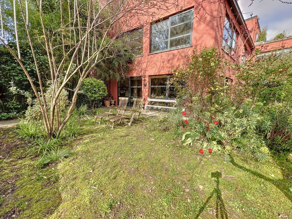 Maison rouge moderne dans un jardin verdoyant, espace paisible et propice à la détente en nature.