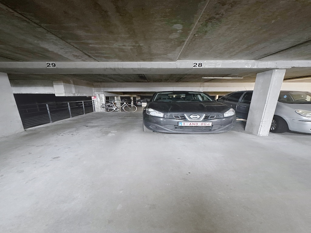Parking souterrain minimaliste en béton avec voitures, vélo, éclairage uniforme et espace organisé.