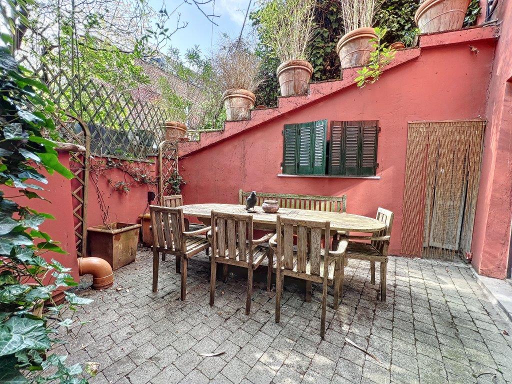 Patio ensoleillé avec mobilier en bois, mur rouge, plantes, ambiance chaleureuse et conviviale.