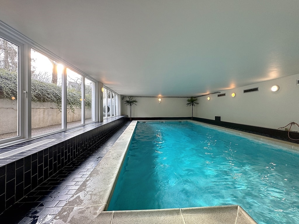 Piscine intérieure moderne avec jardin tropical, luminosité naturelle et design épuré pour relaxation.