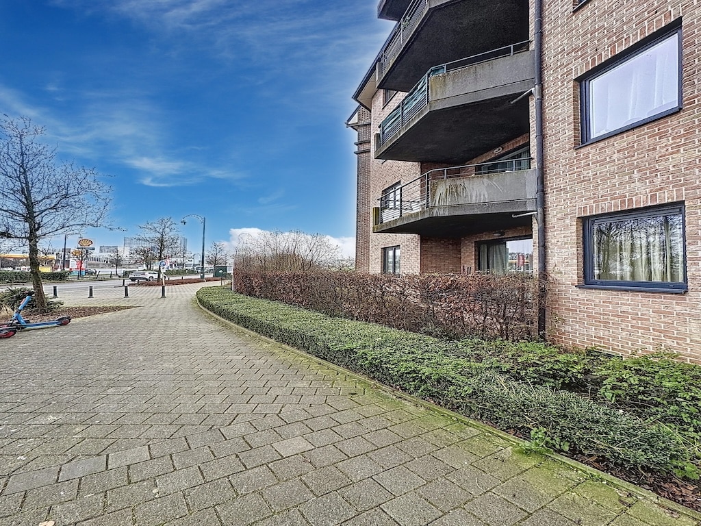 Résidence moderne en brique avec balcons, jardins urbains, allée pavée et vue panoramique.