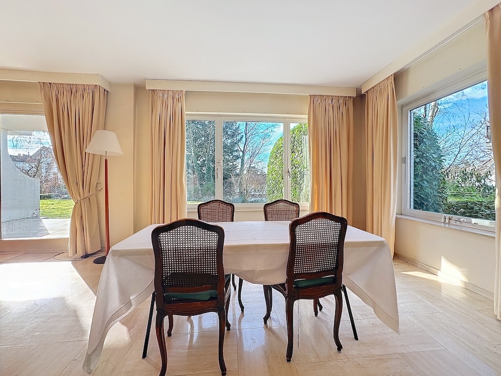 Salle à manger lumineuse avec vue sur jardin, mobilier blanc et bois, ambiance cosy et moderne.