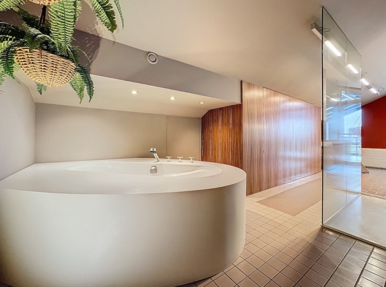 Salle de bain moderne avec baignoire ronde, bois, plante verte et luminosité naturelle.