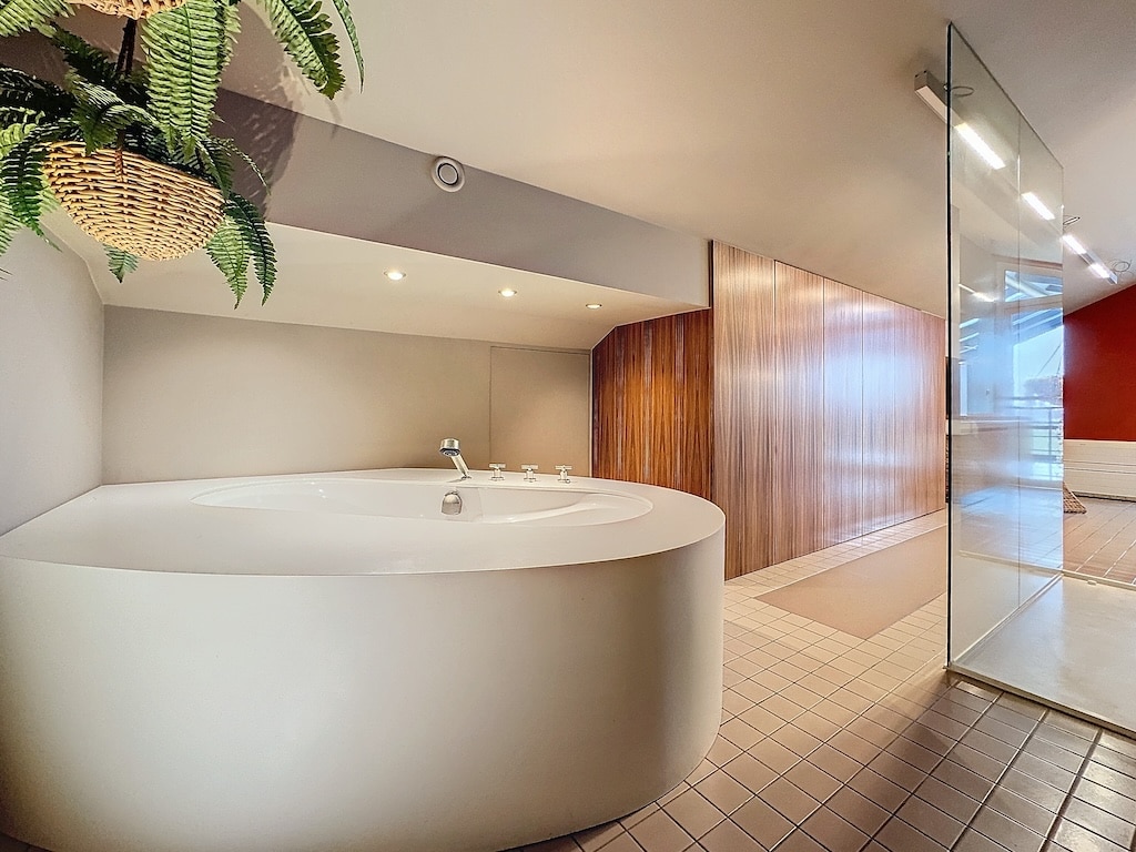 Salle de bain moderne avec baignoire ronde, bois, plante verte et luminosité naturelle.