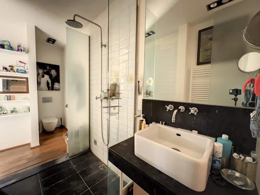 Salle de bain moderne avec douche en verre, vasque blanche, grand miroir éclairé et design épuré.