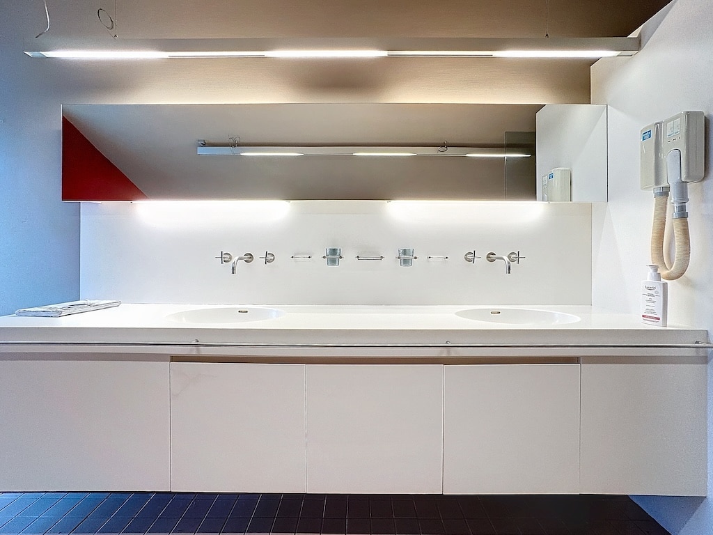 Salle de bain moderne, double vasques, éclairage LED, mur rouge, sols sombres, design épuré et pratique.