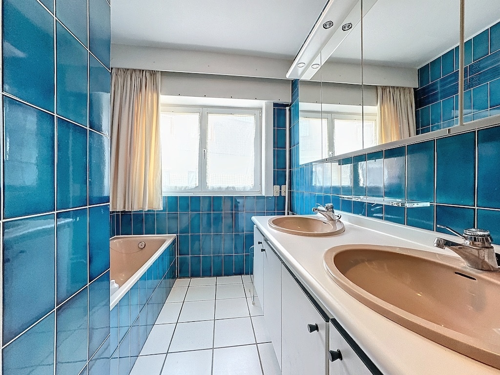 Salle de bain moderne bleue avec double vasque, baignoire, lumière naturelle et design épuré.