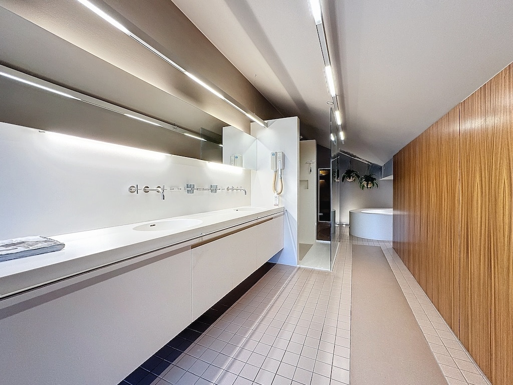 Salle de bain moderne avec lavabo blanc, baignoire arrondie, murs en bois et sol clair.