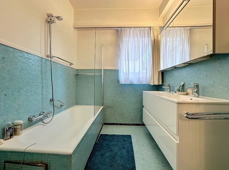 Salle de bain moderne aux tons bleus, baignoire, douche, meuble minimaliste et lumière naturelle.