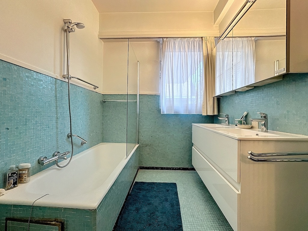 Salle de bain moderne aux tons bleus, baignoire, douche, meuble minimaliste et lumière naturelle.