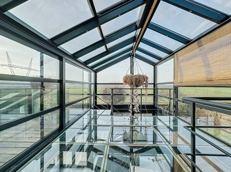 Salle moderne en verre avec vue sur nature, chandelier élégant, ambiance sereine et lumineuse.