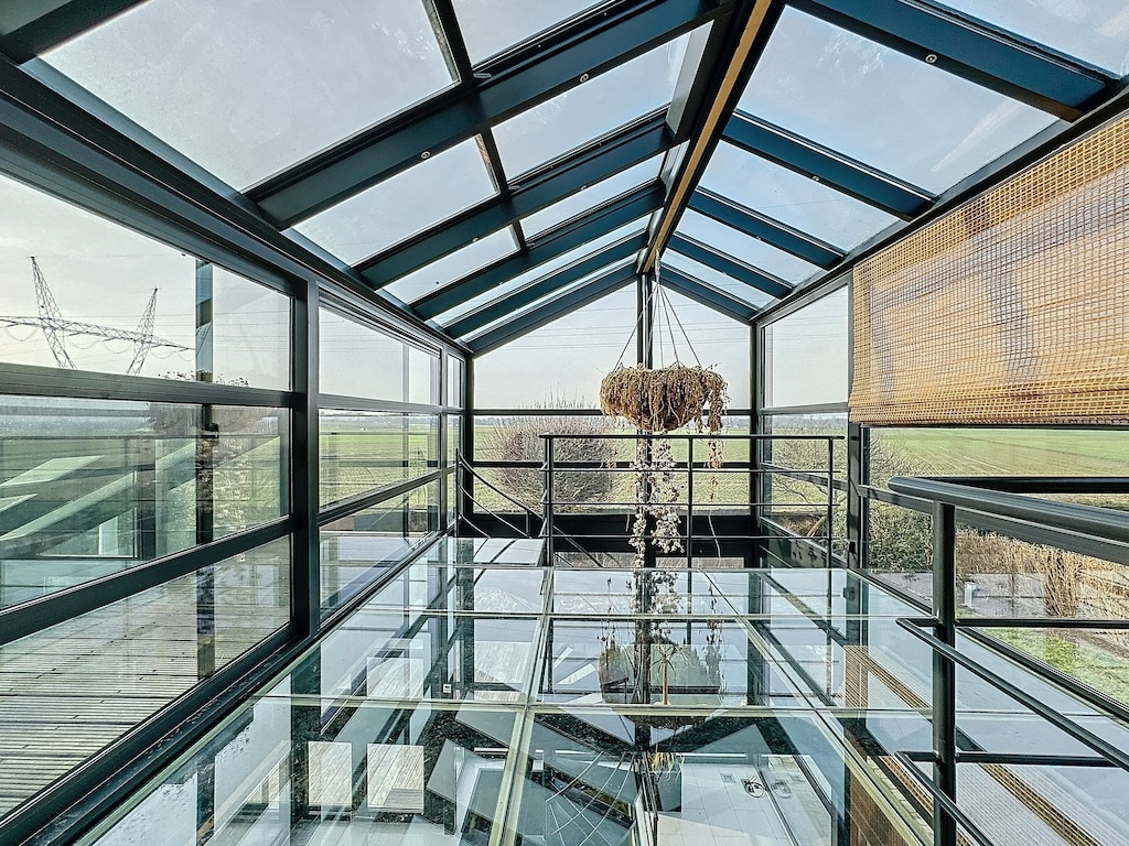 Salle moderne en verre avec vue sur nature, chandelier élégant, ambiance sereine et lumineuse.