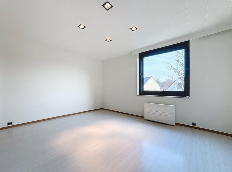 Salle lumineuse moderne avec grands fenêtres, murs blancs, sol clair, et éclairage encastré.