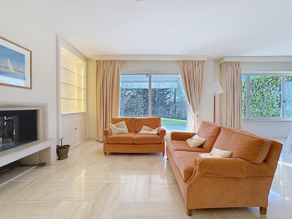 Salon contemporain lumineux avec mobilier orange, cheminée moderne et vue sur jardin verdoyant.