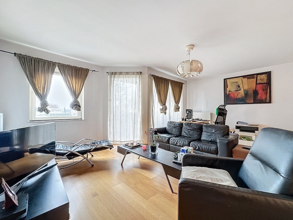 Salon moderne lumineux avec canapé en cuir noir, œuvre abstraite colorée et décoration élégante.