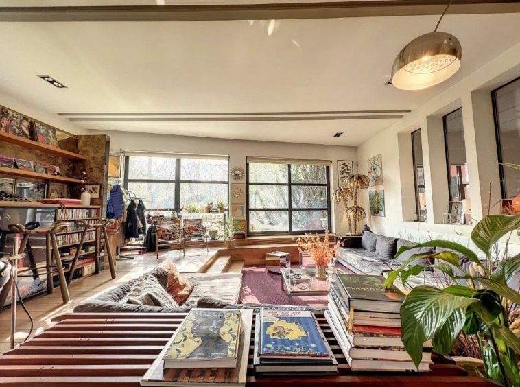 Salon moderne avec bibliothèque, plantes d’intérieur, espace cosy et luminosité naturelle.