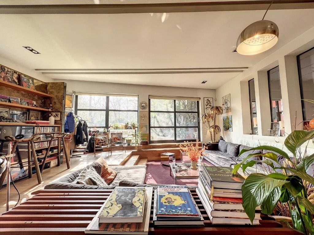 Salon moderne avec bibliothèque, plantes d’intérieur, espace cosy et luminosité naturelle.