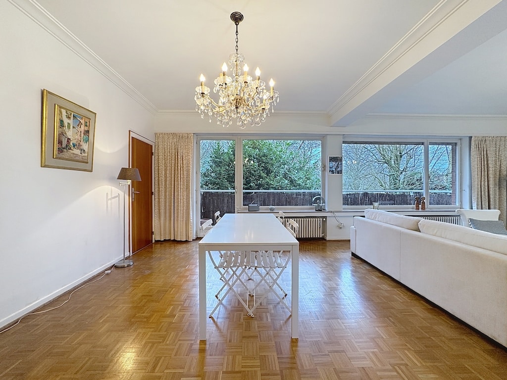 Salon lumineux avec chandelier en cristal, mobilier moderne et vue verdoyante.