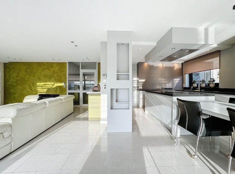 Salon moderne avec cuisine ouverte, mobilier blanc, mur vert lime, espace lumineux et convivial.