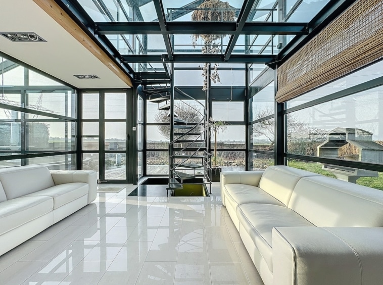 Salon moderne lumineux avec escalier en spirale, vue sur jardin et intérieur minimaliste en verre.