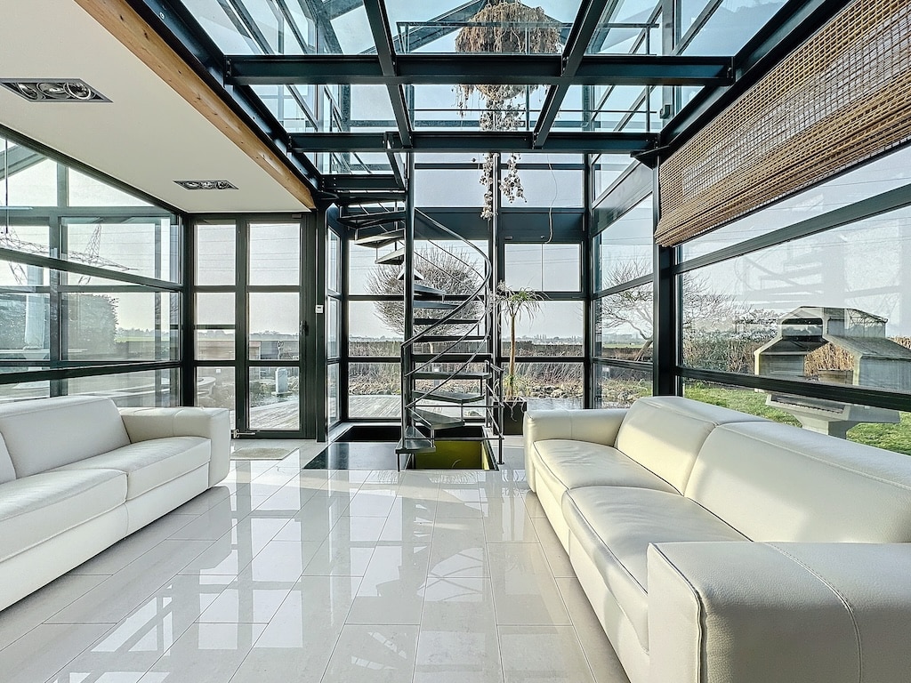 Salon moderne lumineux avec escalier en spirale, vue sur jardin et intérieur minimaliste en verre.