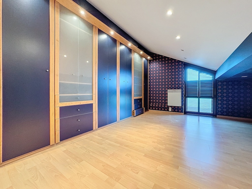 Salon moderne lumineux avec mur bleu, bibliothèque en bois et éclairage LED intégré.