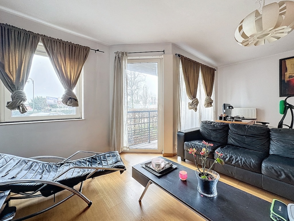 Salon moderne et cosy avec espace de travail, lumière naturelle, canapé noir et décoration élégante.