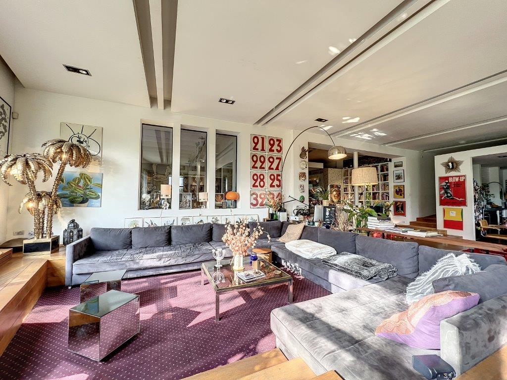 Salon moderne avec canapé gris, art numérique, déco éclectique et lumière naturelle abondante.