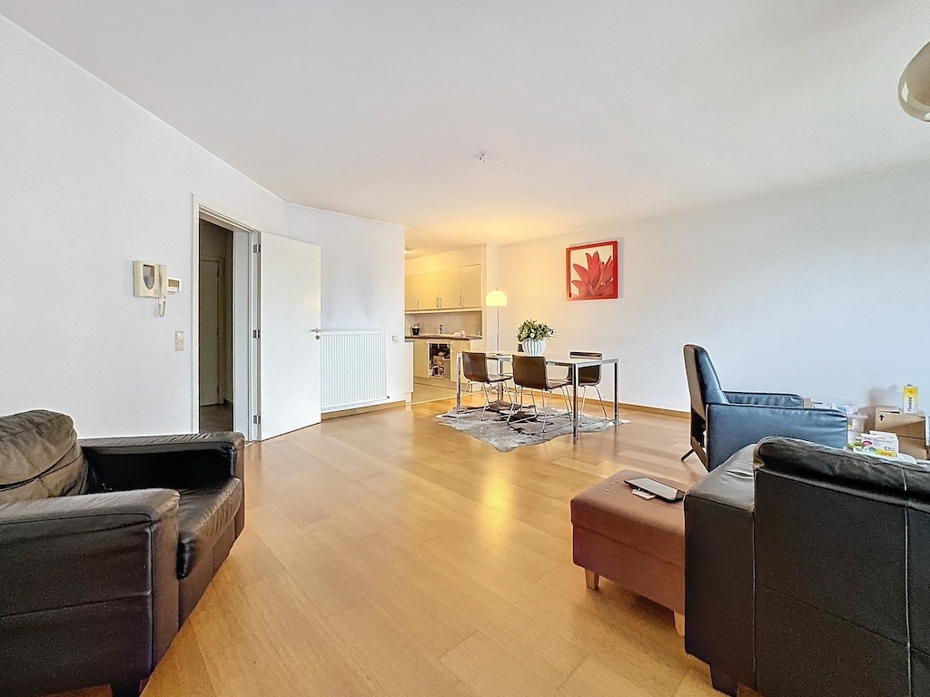 Salon moderne cosy avec mobilier en cuir, table en verre, cuisine ouverte lumineuse.